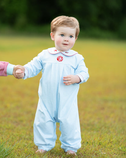Child wearing a light blue outfit with a red monogram in a grassy field