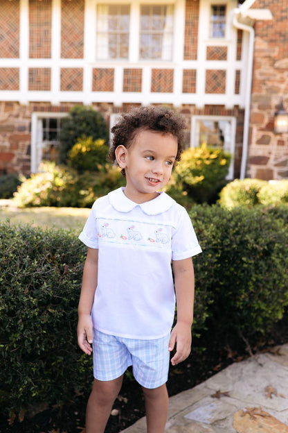 Child wearing a light blue polo shirt with a collar and plaid shorts standing outdoors.
