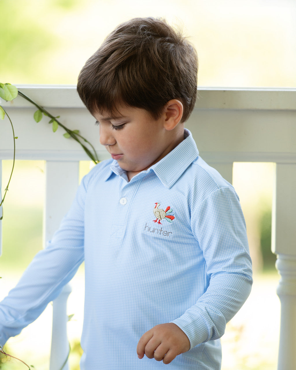 Child wearing a light blue polo shirt with an embroidered turkey standing outdoors