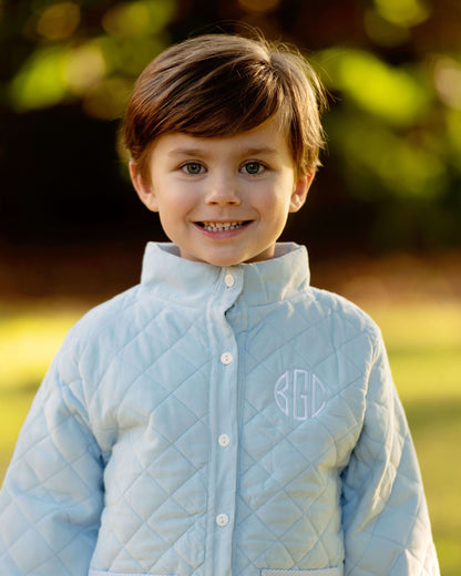 Child wearing a light blue quilted jacket with a monogram, standing outdoors.