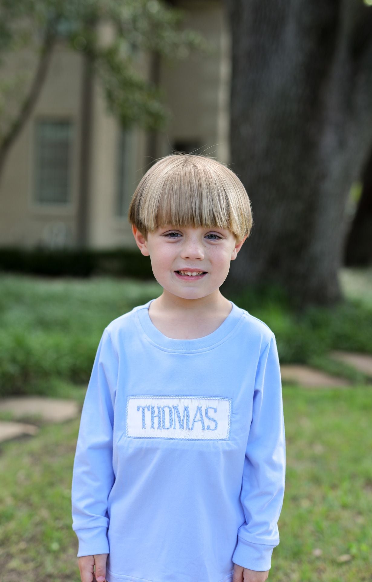 Child wearing a light blue shirt with 'THOMAS' printed on it, standing outdoors.