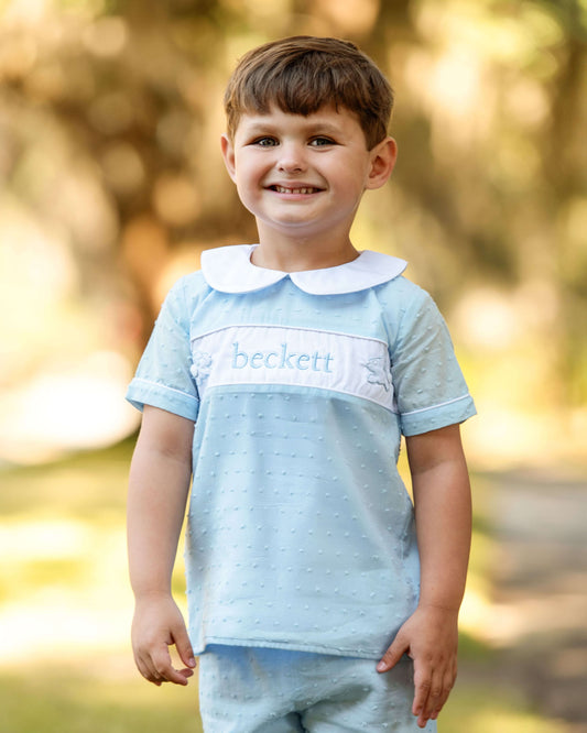 Child wearing a light blue shirt with a collar and 'beckett' branding, standing outdoors.