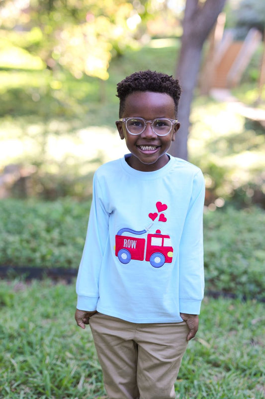 Child wearing a light blue shirt with a red fire truck design outdoors