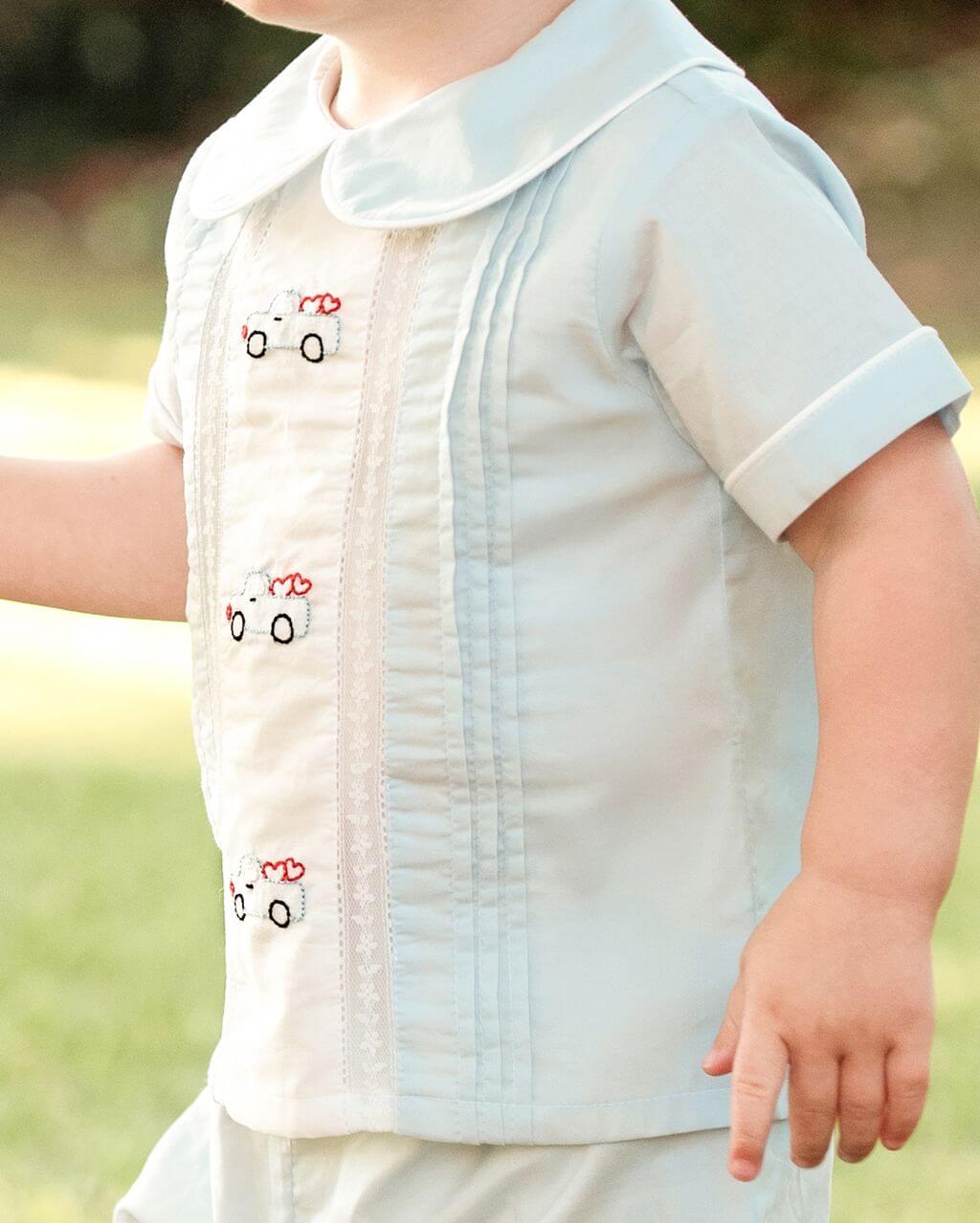 Child wearing a light blue shirt with embroidery and pleats, outdoors