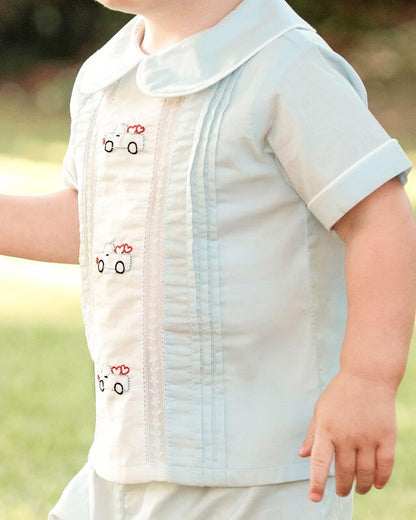 Child wearing a light blue shirt with embroidery and pleats, outdoors
