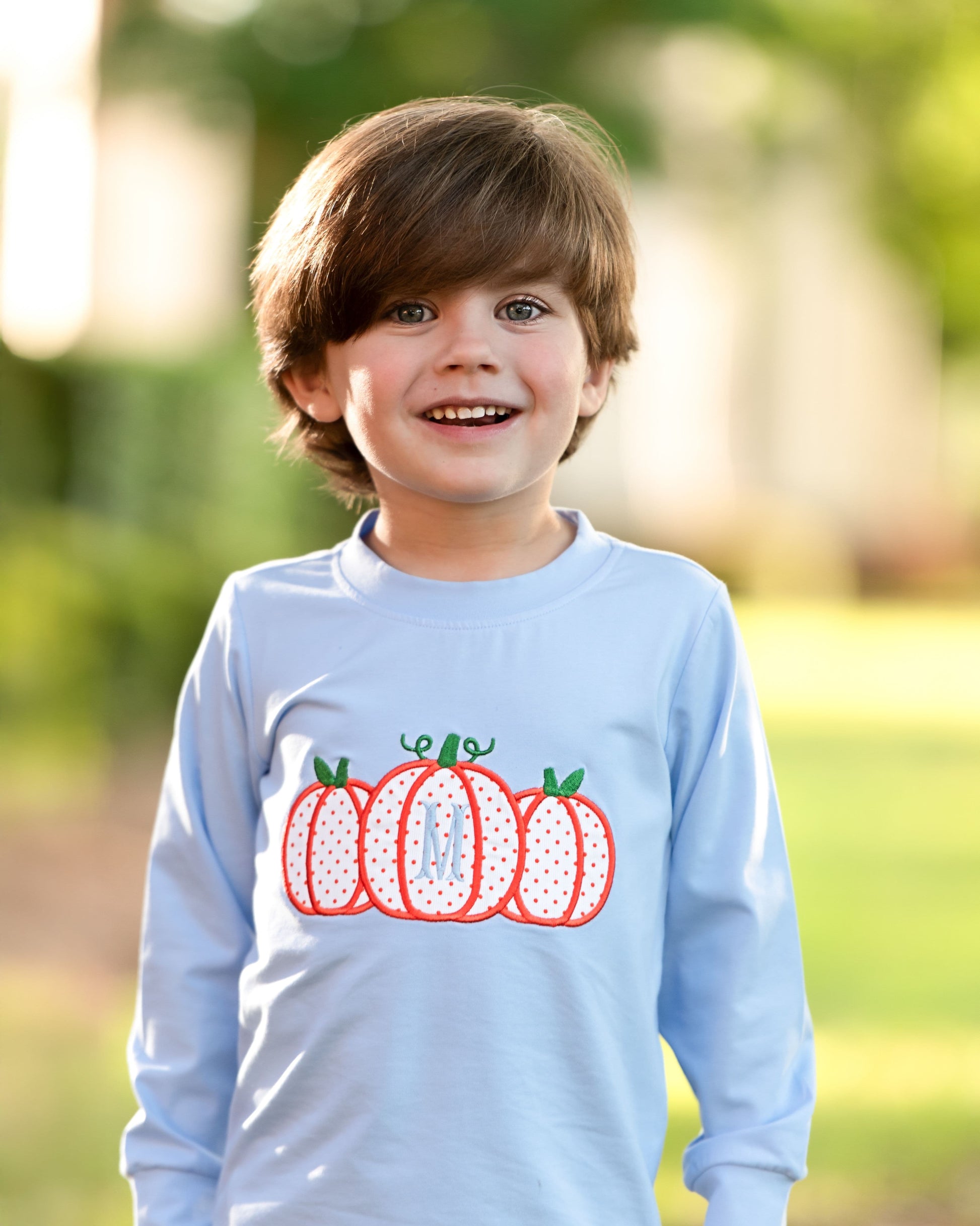 Child wearing a light blue shirt with pumpkin design outdoors