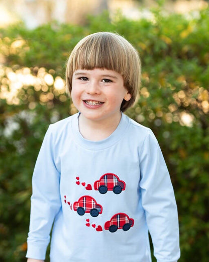 Child wearing a light blue shirt with red car designs outdoors