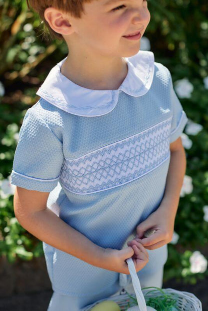 Child wearing a light blue short set with white collar and smocked details, standing outdoors.
