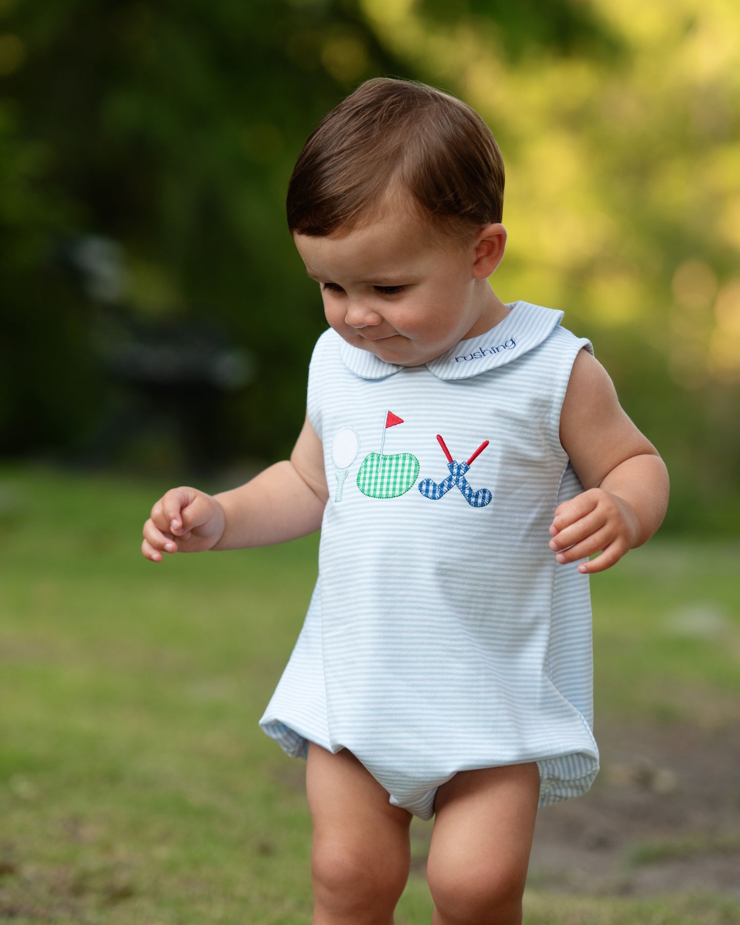 Child wearing a light blue sleeveless dress with a golf-themed design outdoors.