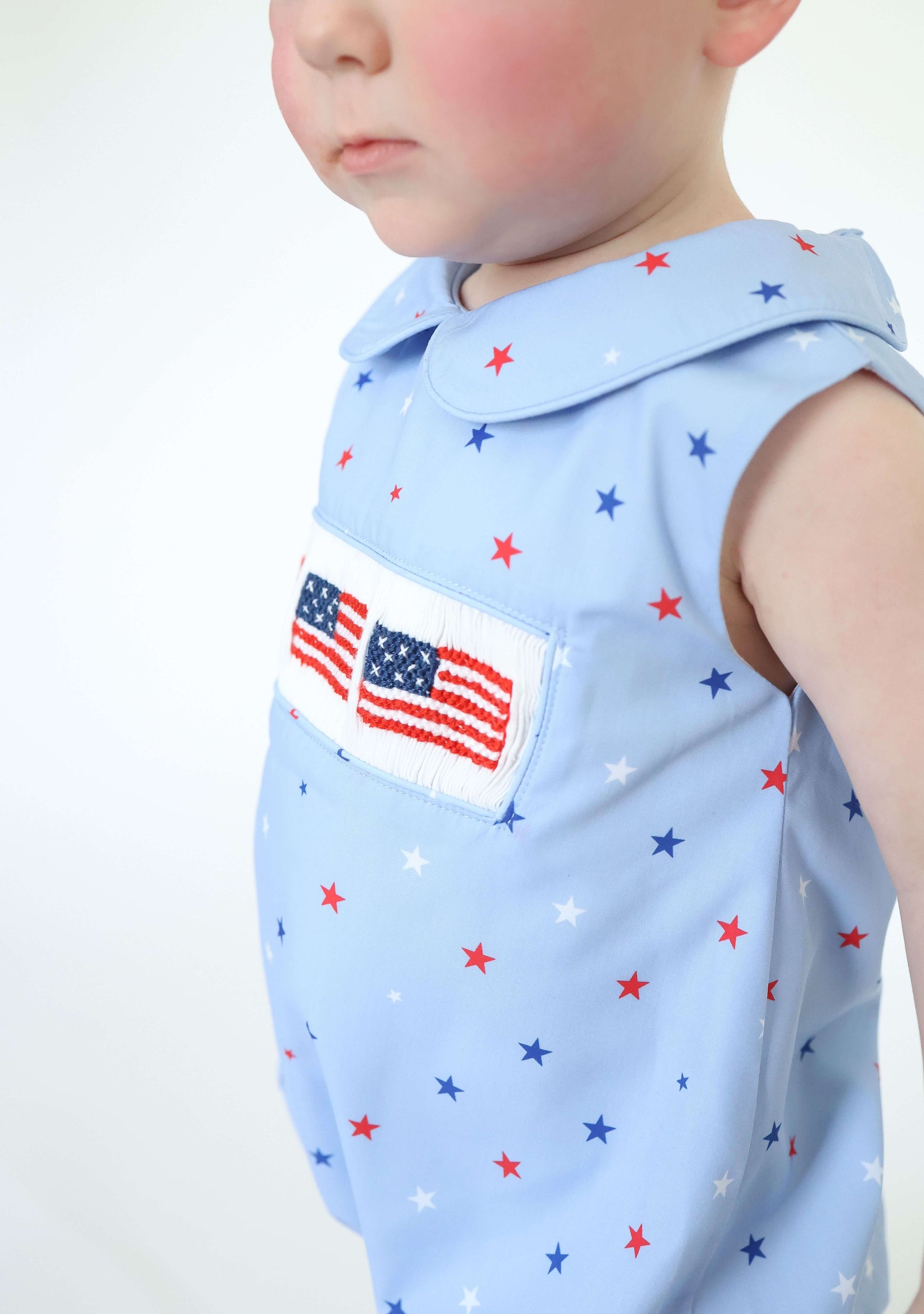 Child wearing a light blue sleeveless shirt with star pattern and American flag patch.