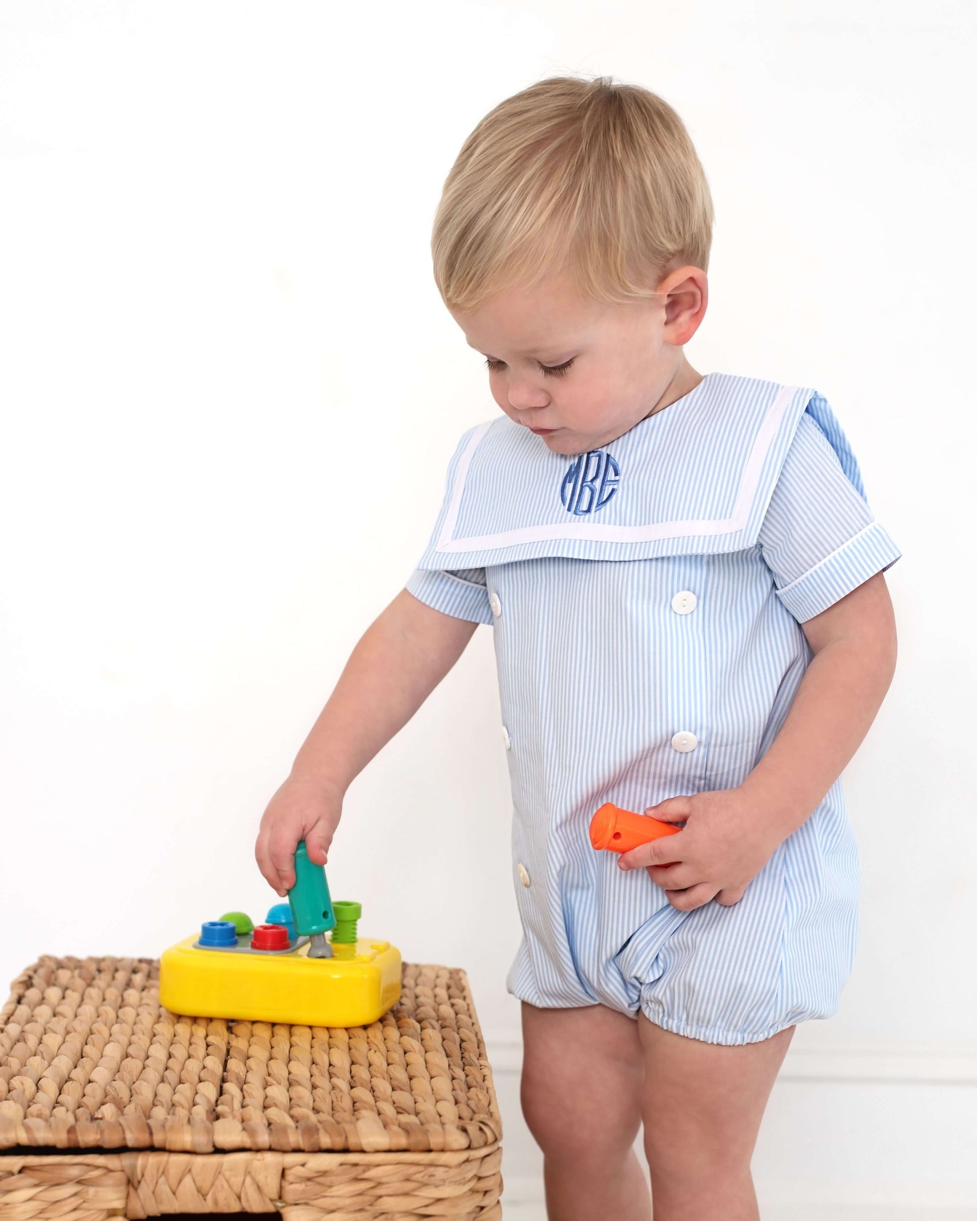 Child wearing a light blue striped bubble playing with toys on a white background
