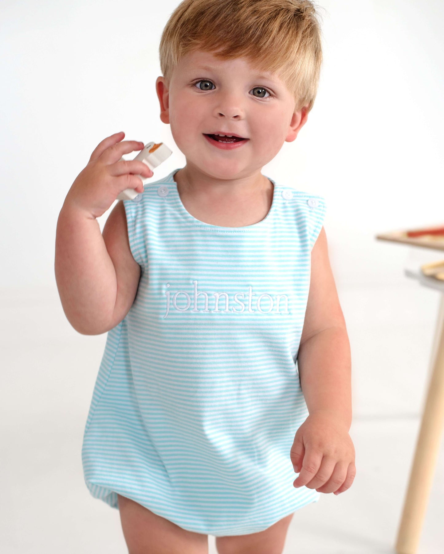 Child wearing a light blue striped dress with 'Johnston' printed on it, standing against a white background.