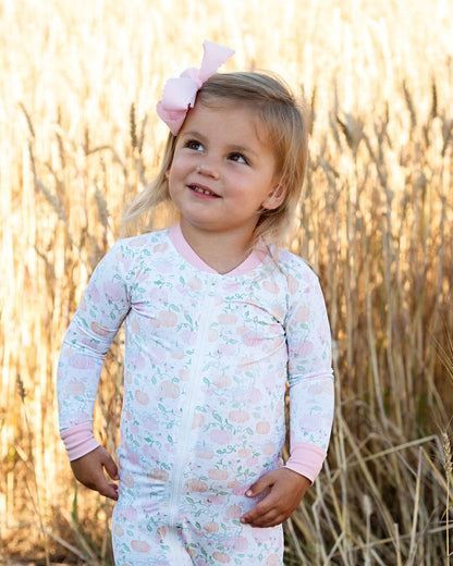 Child wearing a light pink and white pumpkin patterned outfit with a bow in a field.