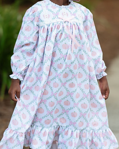 Child wearing a long-sleeve night gown with pink pumpkins on a light blue background.