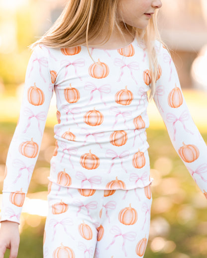Child wearing a long-sleeve shirt with orange pumpkin pattern on a blurred outdoor background