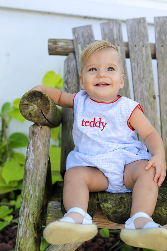 Child wearing a monogrammed onesie sitting on a wooden bench outdoors.