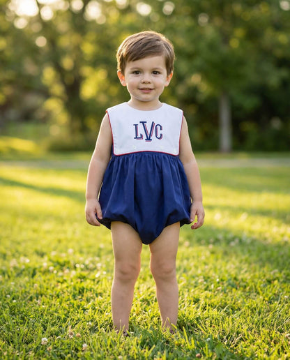 Child wearing a navy and white dress with 'LVC' initials standing on grass.
