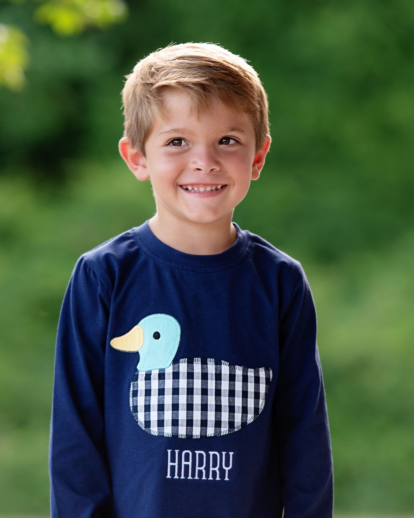Child wearing a navy blue sweatshirt with a duck design and 'HARRY' text, standing outdoors.