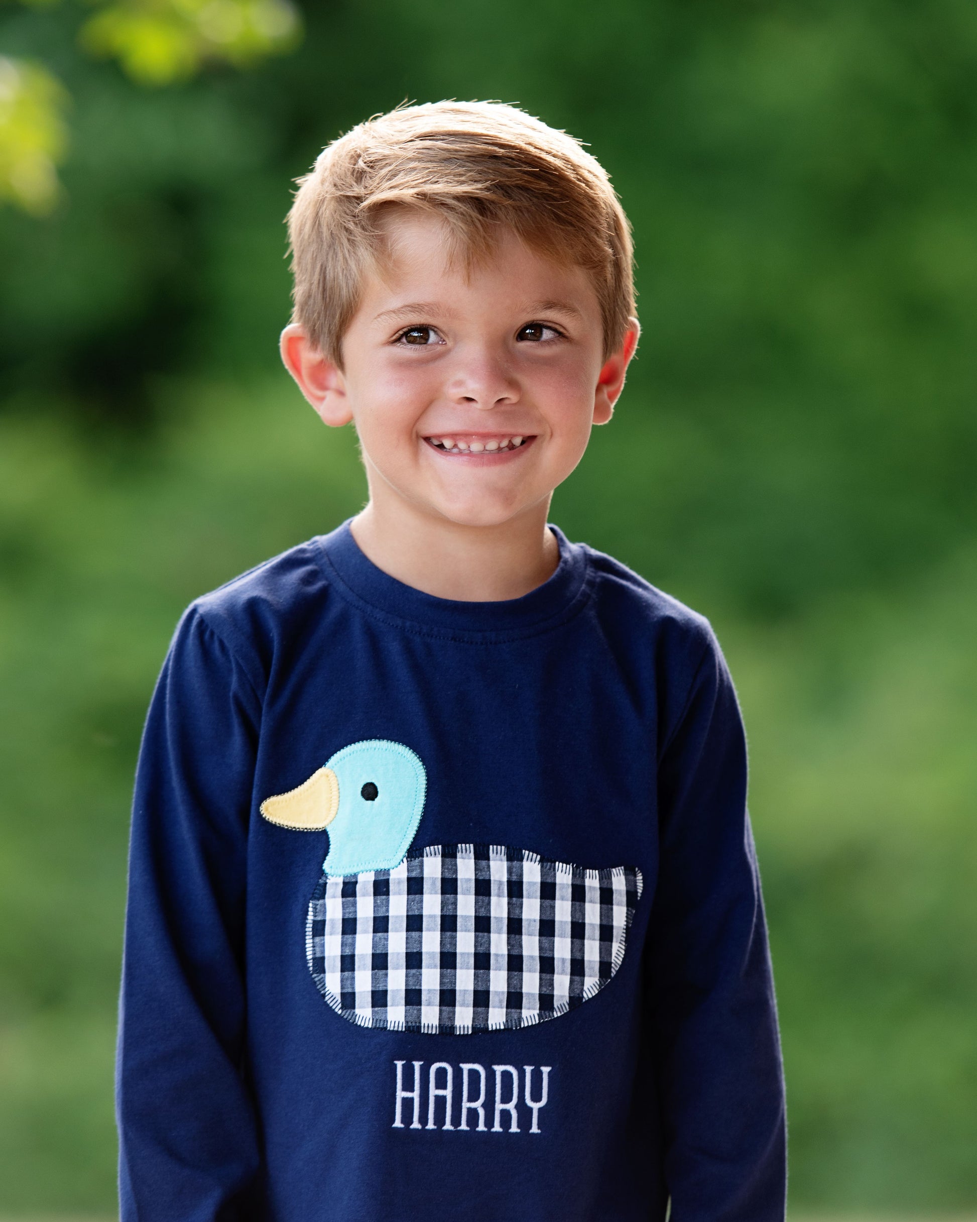 Child wearing a navy blue sweatshirt with a duck design and 'HARRY' text, standing outdoors.