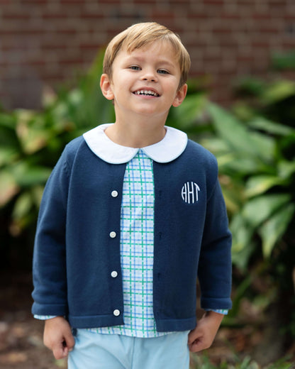 Child wearing a navy cardigan with a white collar and monogram, standing outdoors.