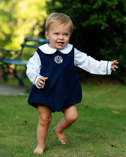 Child wearing a navy dress with a white collar and monogram standing on grass 1