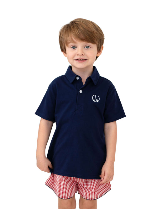 Child wearing a navy polo shirt and red checkered shorts on a white background