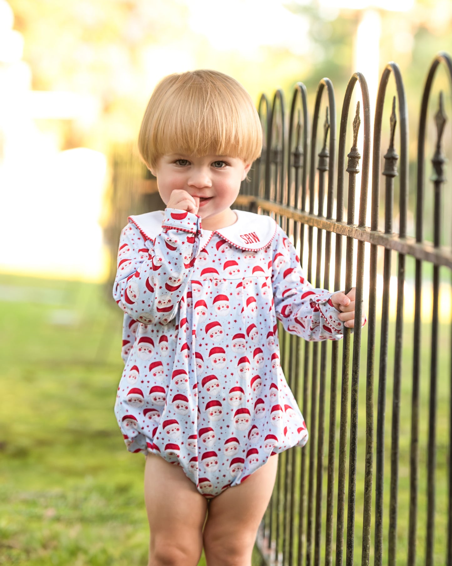 Child wearing a patterned onesie standing in front of a black metal fence.