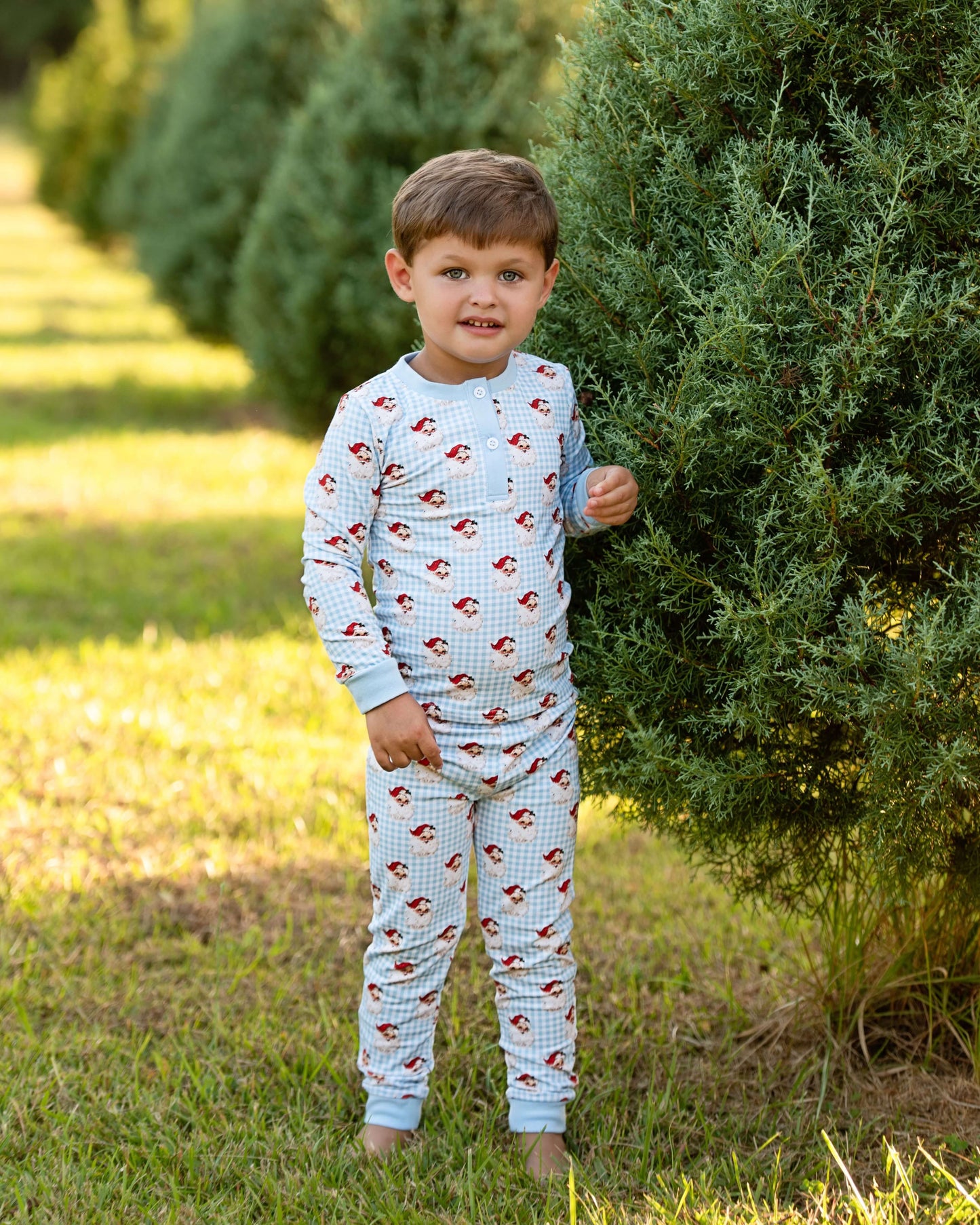 Child wearing a patterned outfit standing outdoors near green bushes.