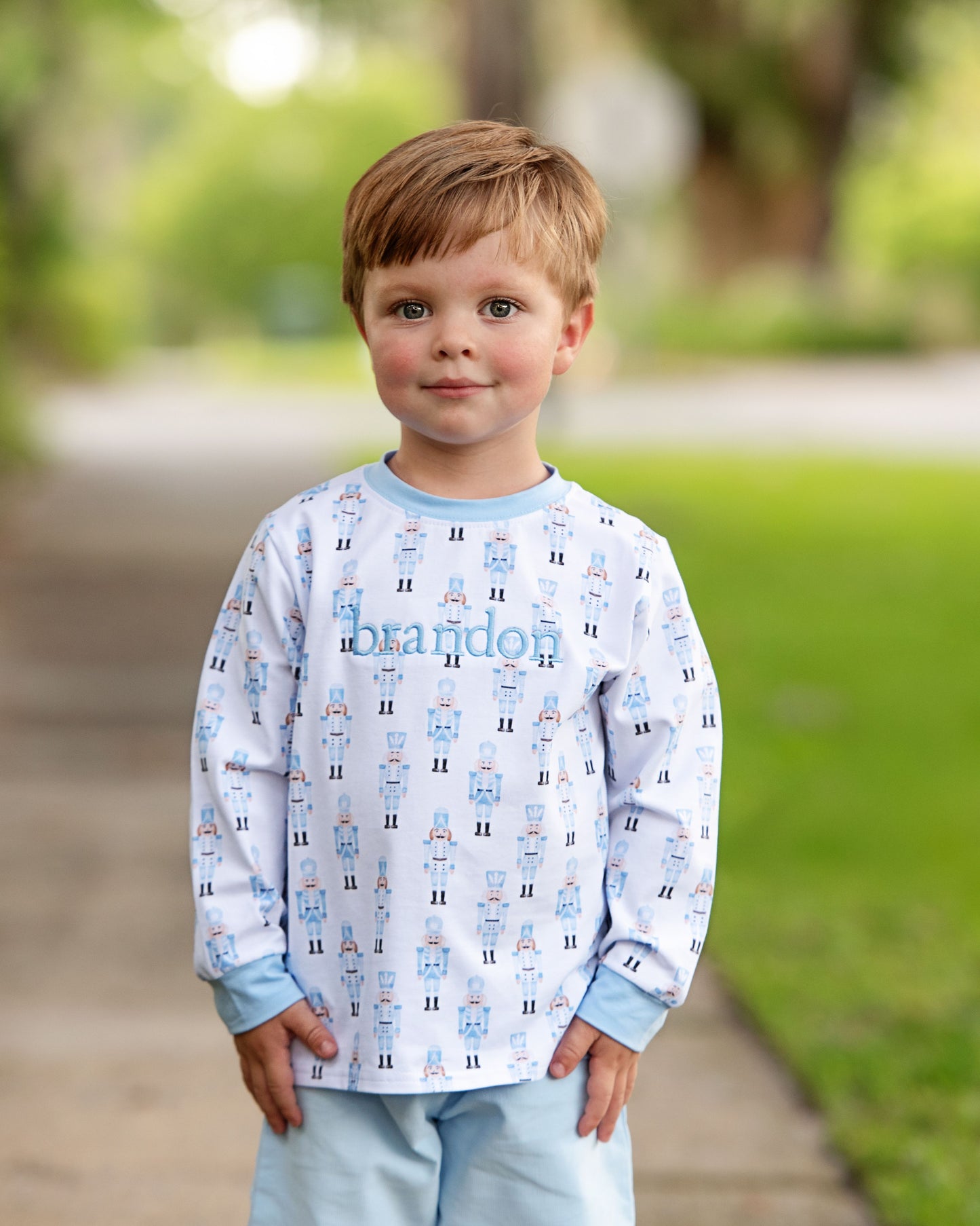 Child wearing a patterned shirt with 'brandon' printed on it, standing outdoors.