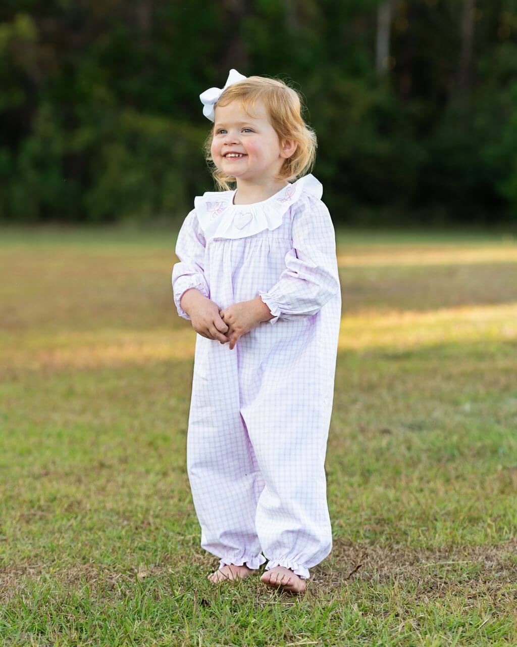 Child wearing a pink and white outfit with a bow in a grassy field