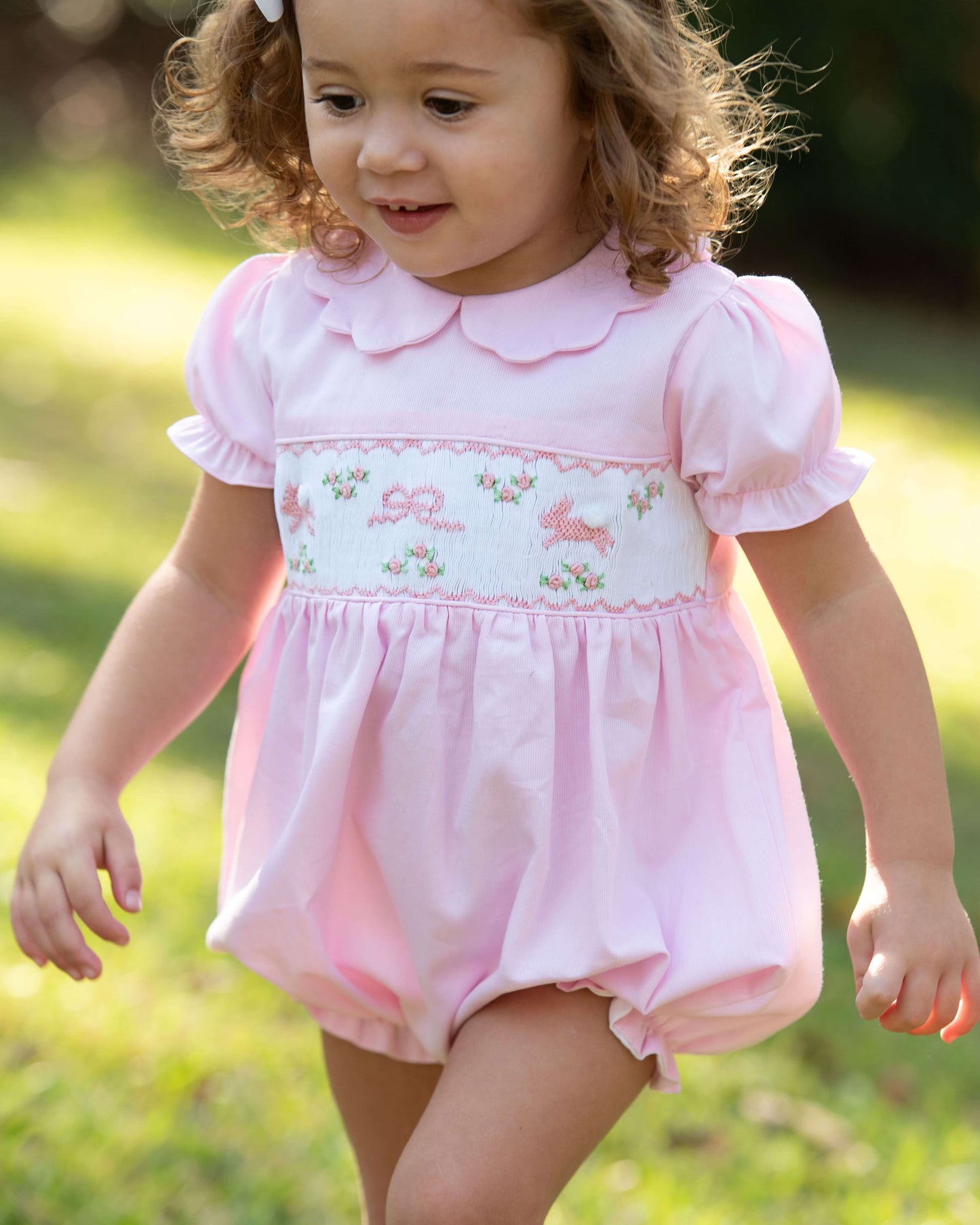 Child wearing a pink bubble with smocked bunnies outdoors