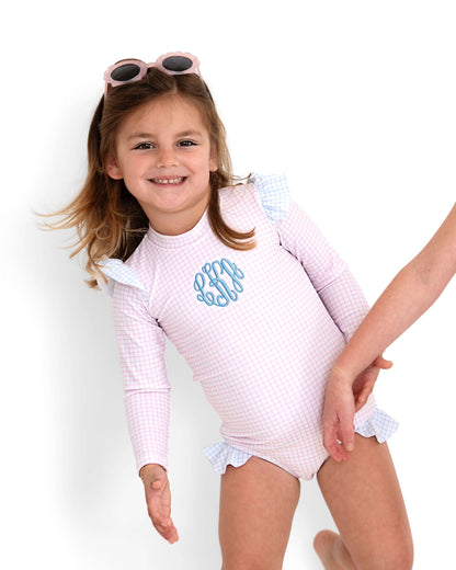 Child wearing a pink checkered swimsuit with ruffles on a white background