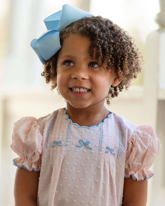 Child wearing a pink dress with blue accents and a large blue bow in her hair.