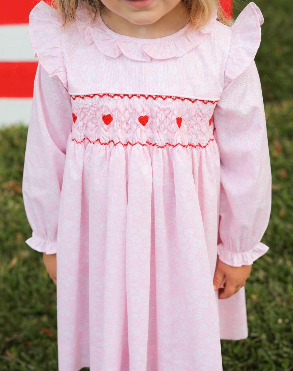 Child wearing a pink dress with red heart details against a grassy background