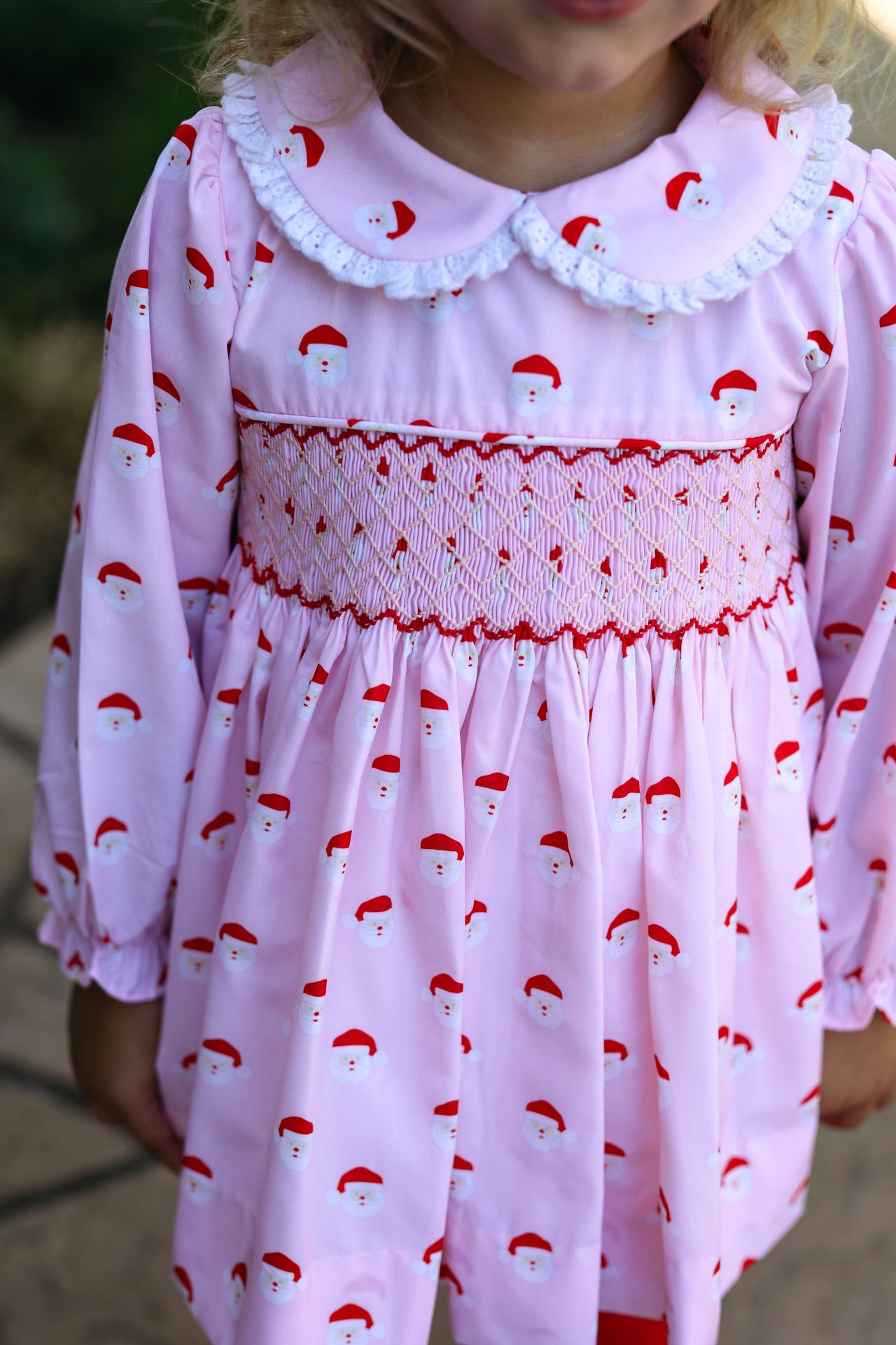 Child wearing a pink dress with red patterns and white collar.