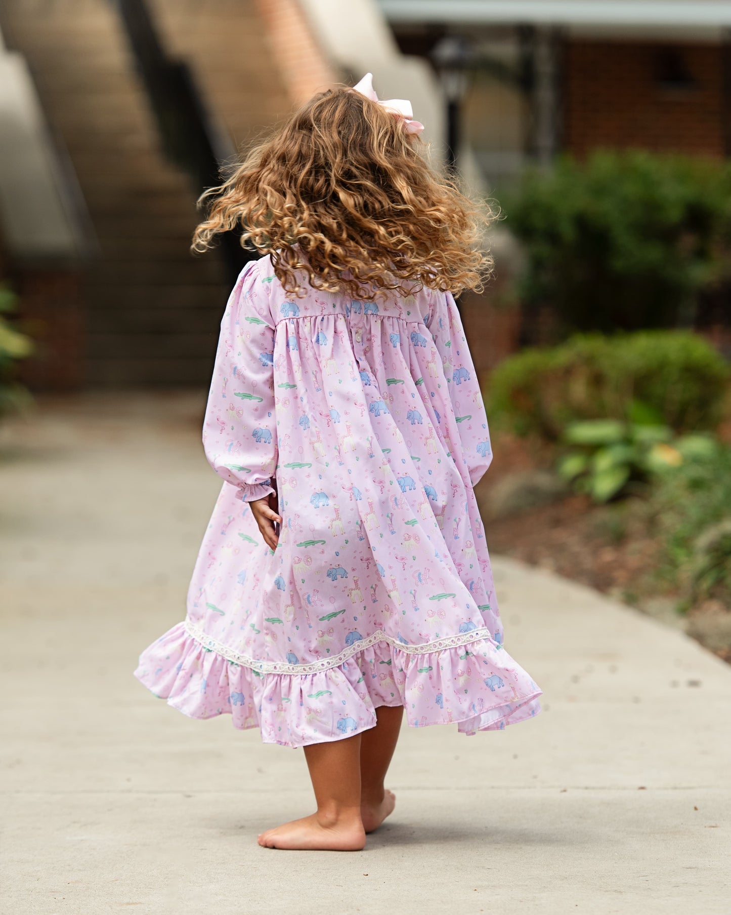 Child wearing a pink floral birthday nightgown standing on a sidewalk.