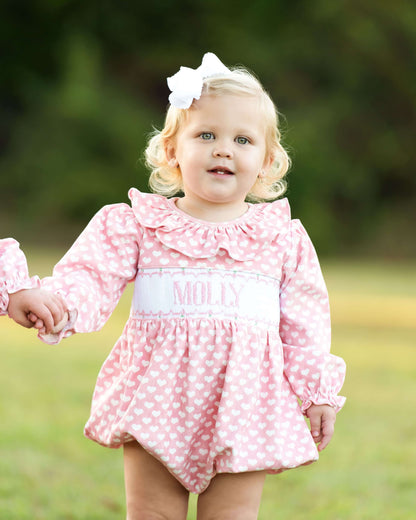 Child wearing a pink heart bubble with 'Molly' monogrammed on it, standing outdoors.