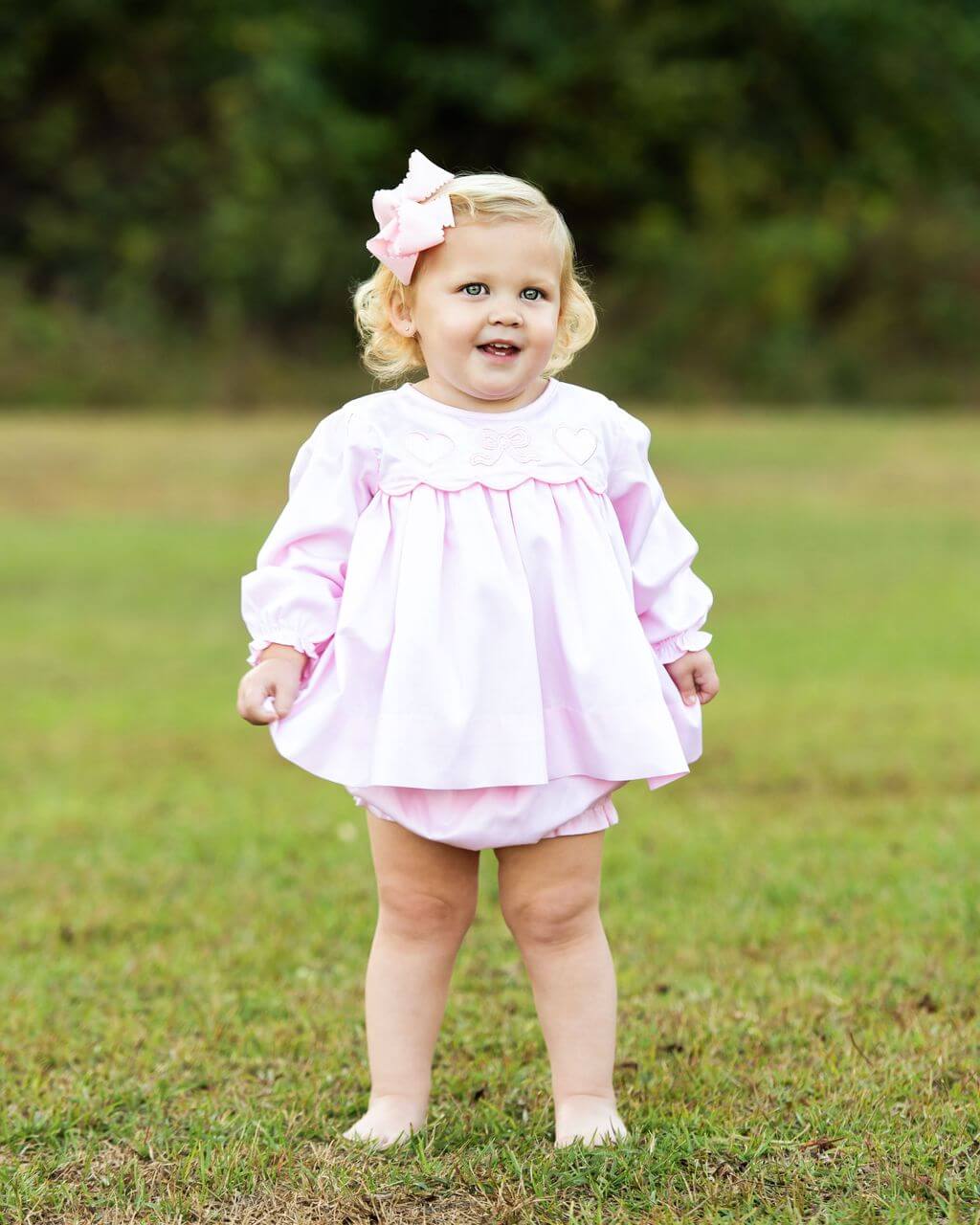 Child wearing a pink outfit with a bow in a grassy field
