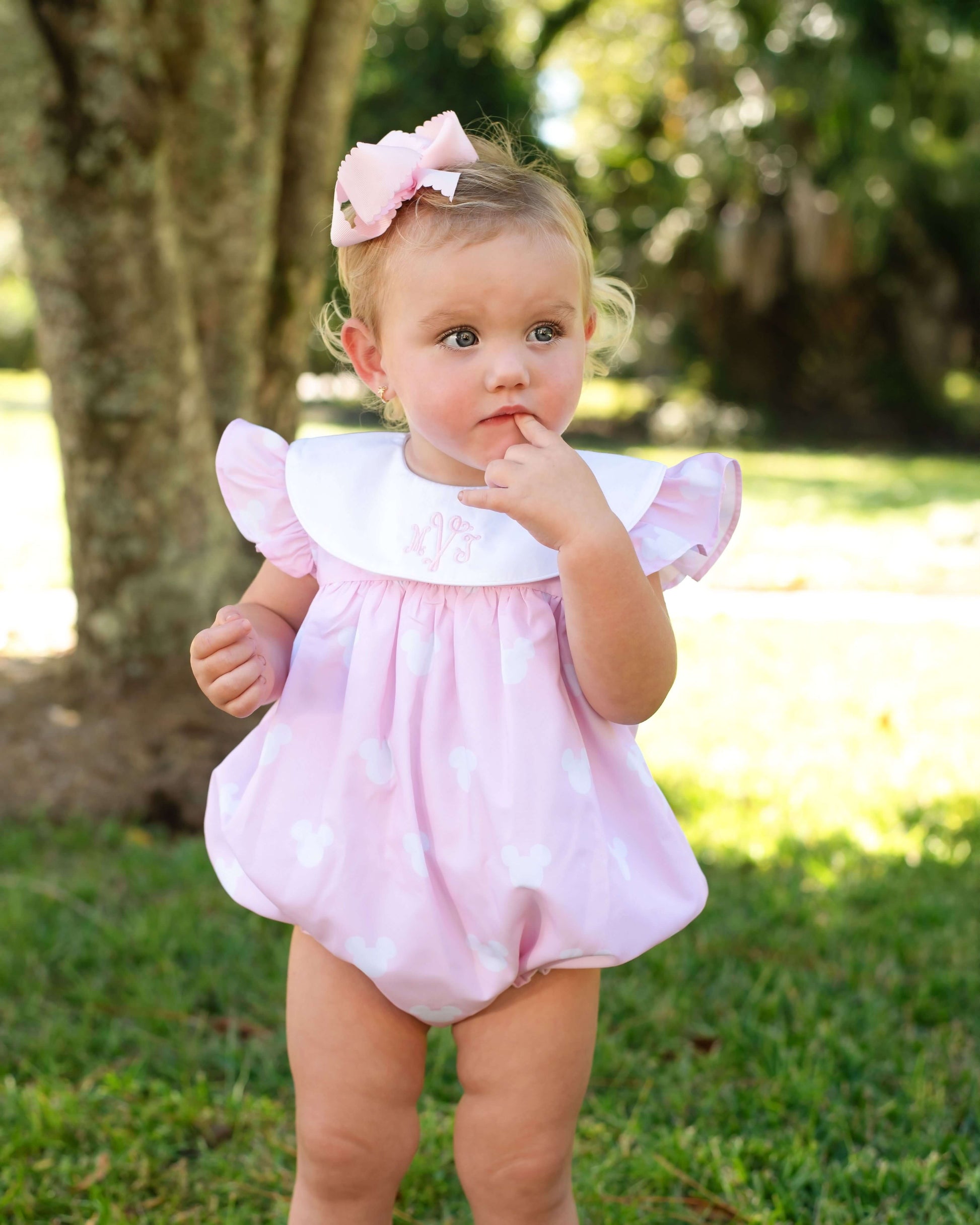 Child wearing a pink outfit with ruffled sleeves and collar, standing outdoors.
