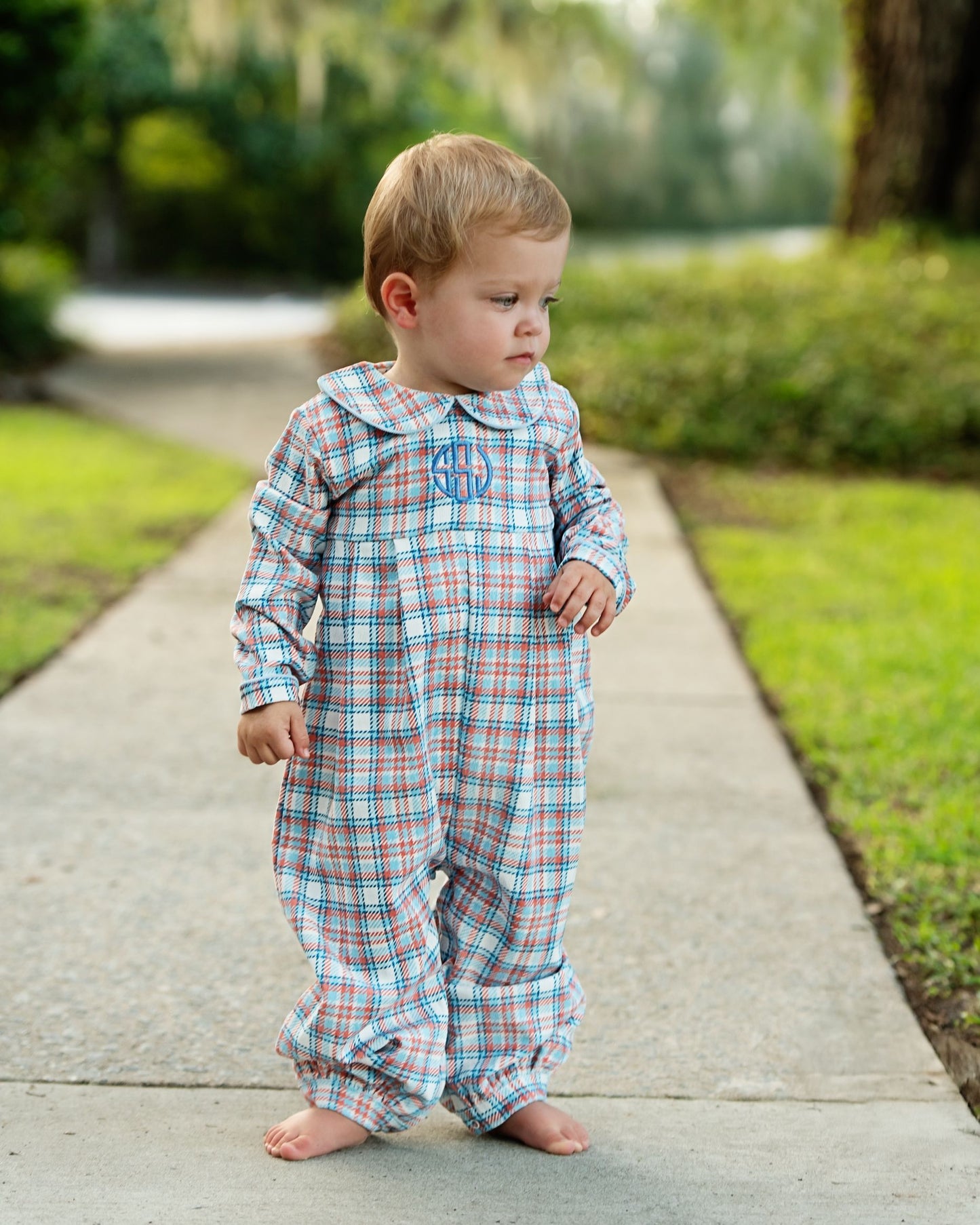 Child wearing a plaid outfit with a monogram on a sidewalk.