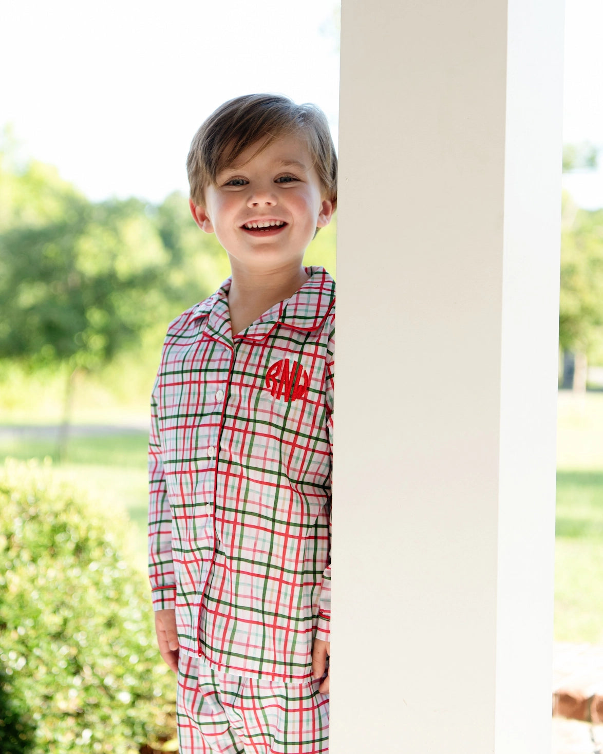 Child wearing a plaid outfit with a red monogram, standing outdoors.