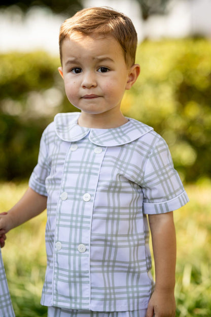 Child wearing a plaid shirt outdoors with greenery in the background