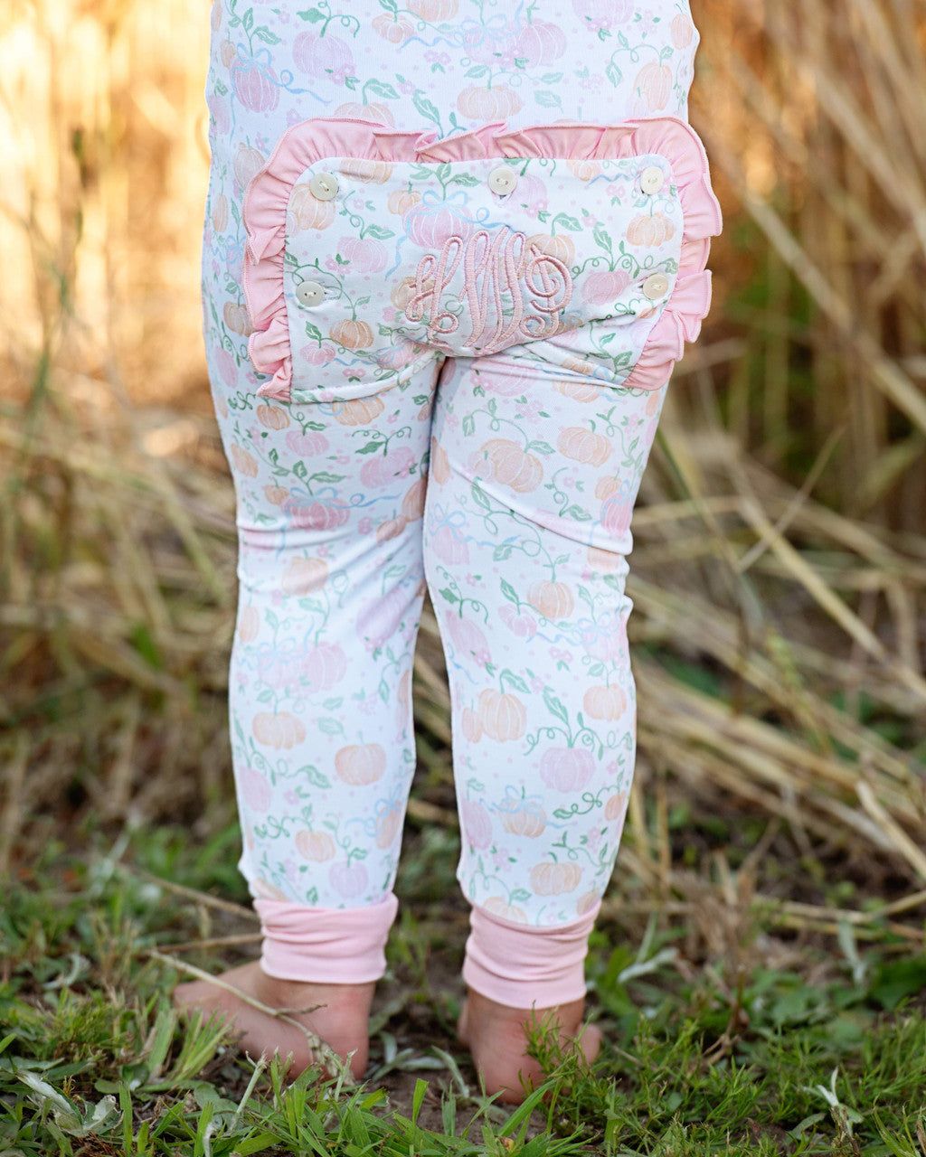 Child wearing a pumpkin patterned outfit with pink accents in a natural setting