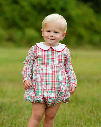 Child wearing a red and green checkered romper with a white collar outdoors.