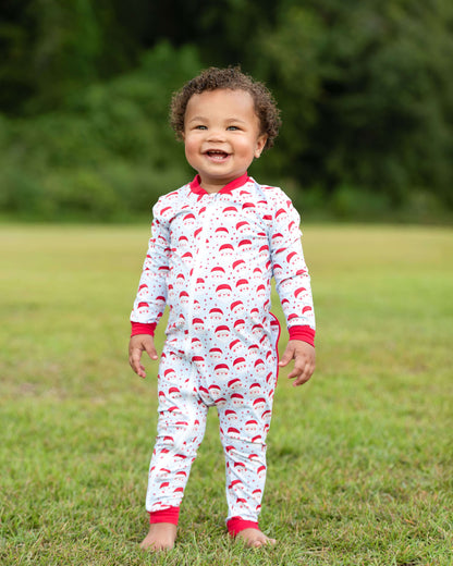 Child wearing a red and white patterned onesie standing in a grassy field.