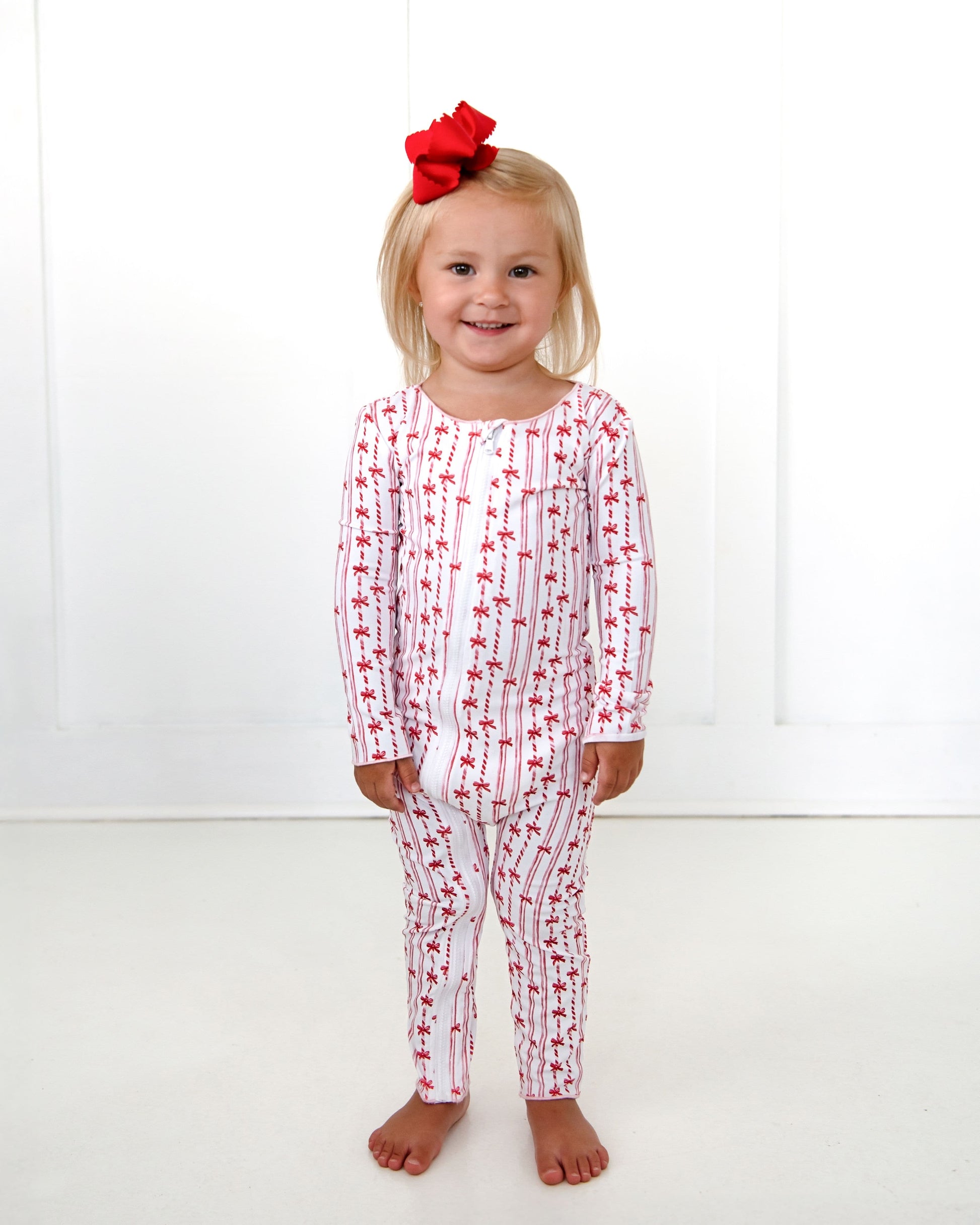 Child wearing a red and white patterned onesie with a red bow on a white background