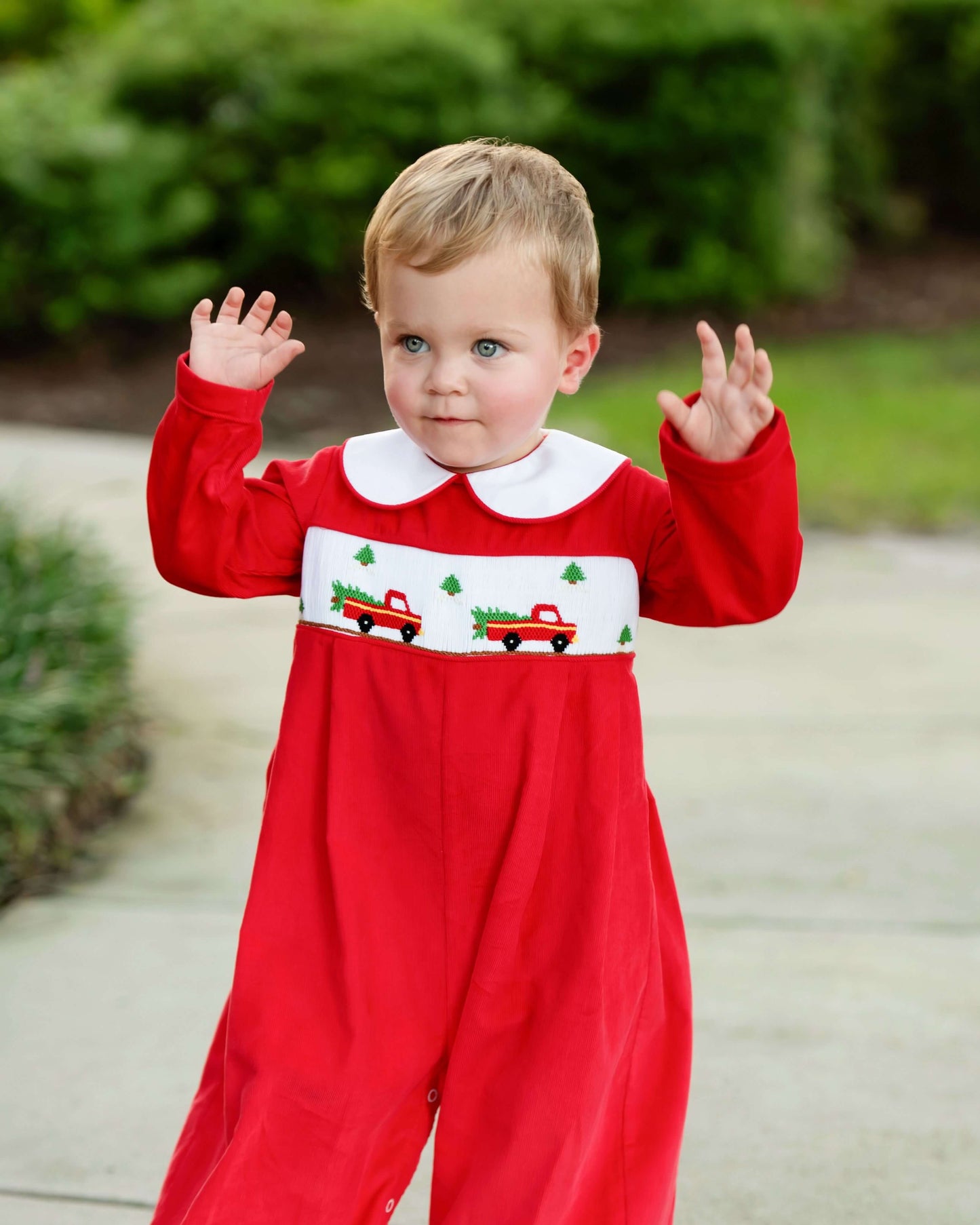 Child wearing a red onesie with Christmas designs outdoors.