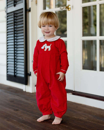 Child wearing a red pajama with a white dog design, standing on a wooden floor.
