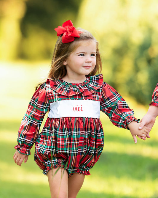 Child wearing a red plaid outfit with a white waistband outdoors.