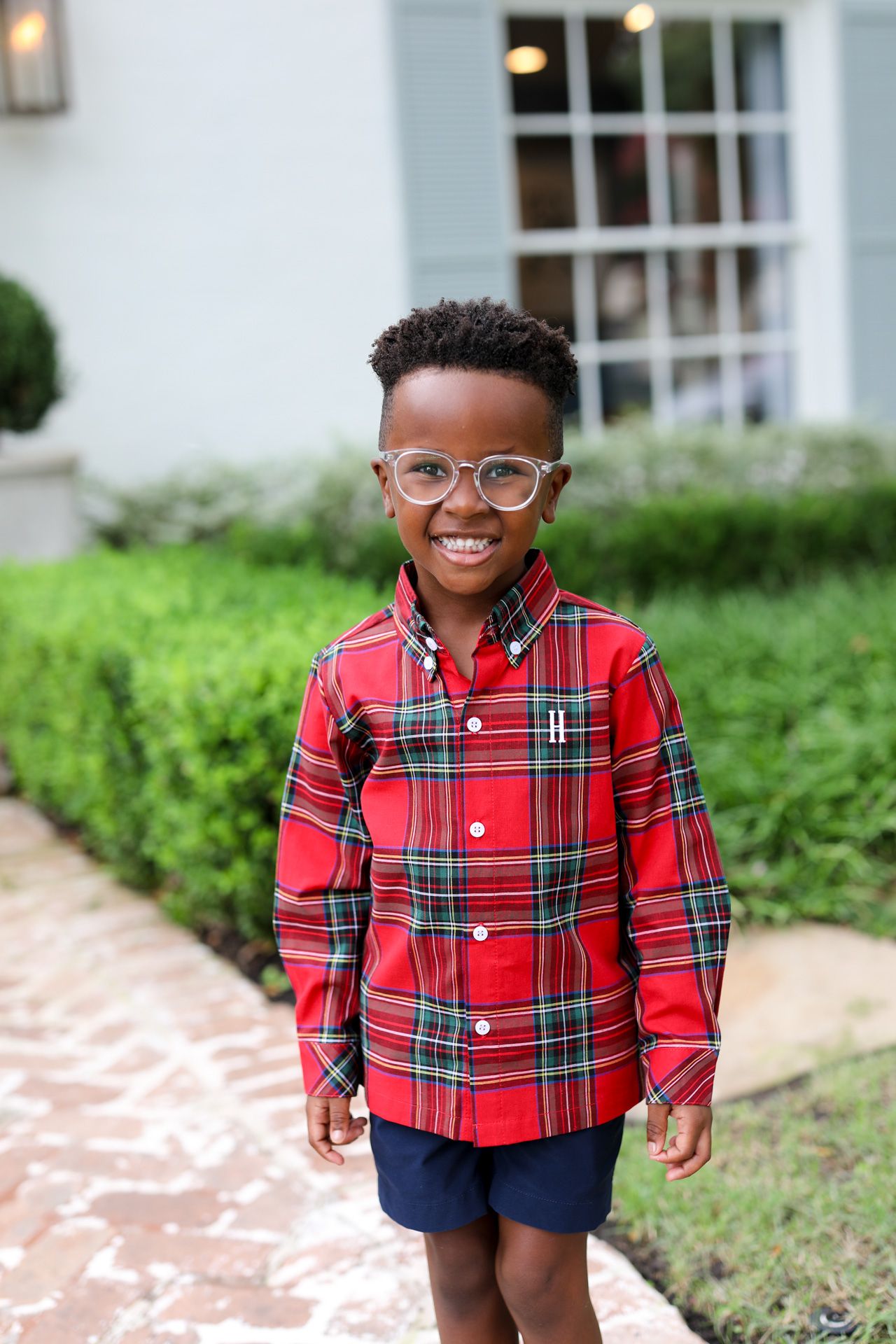 Child wearing a red plaid shirt and glasses standing outdoors.